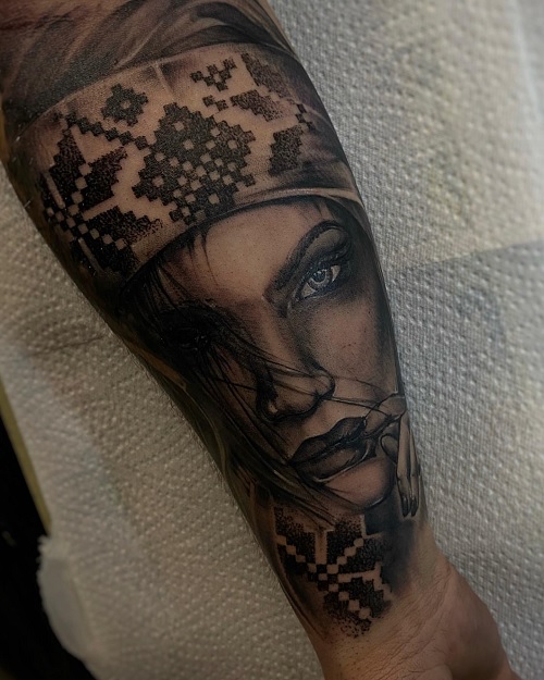 black and grey tattoo arm with detailed portrait of a woman's face combined with a patterned design