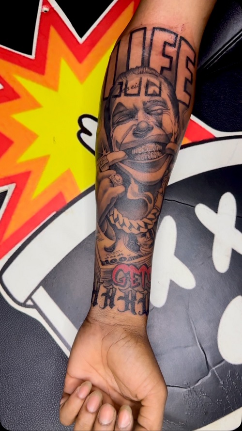 detailed black and grey tattoo on a person's forearm, featuring a stylized rendition of a "Laugh Now, Cry Later" motif